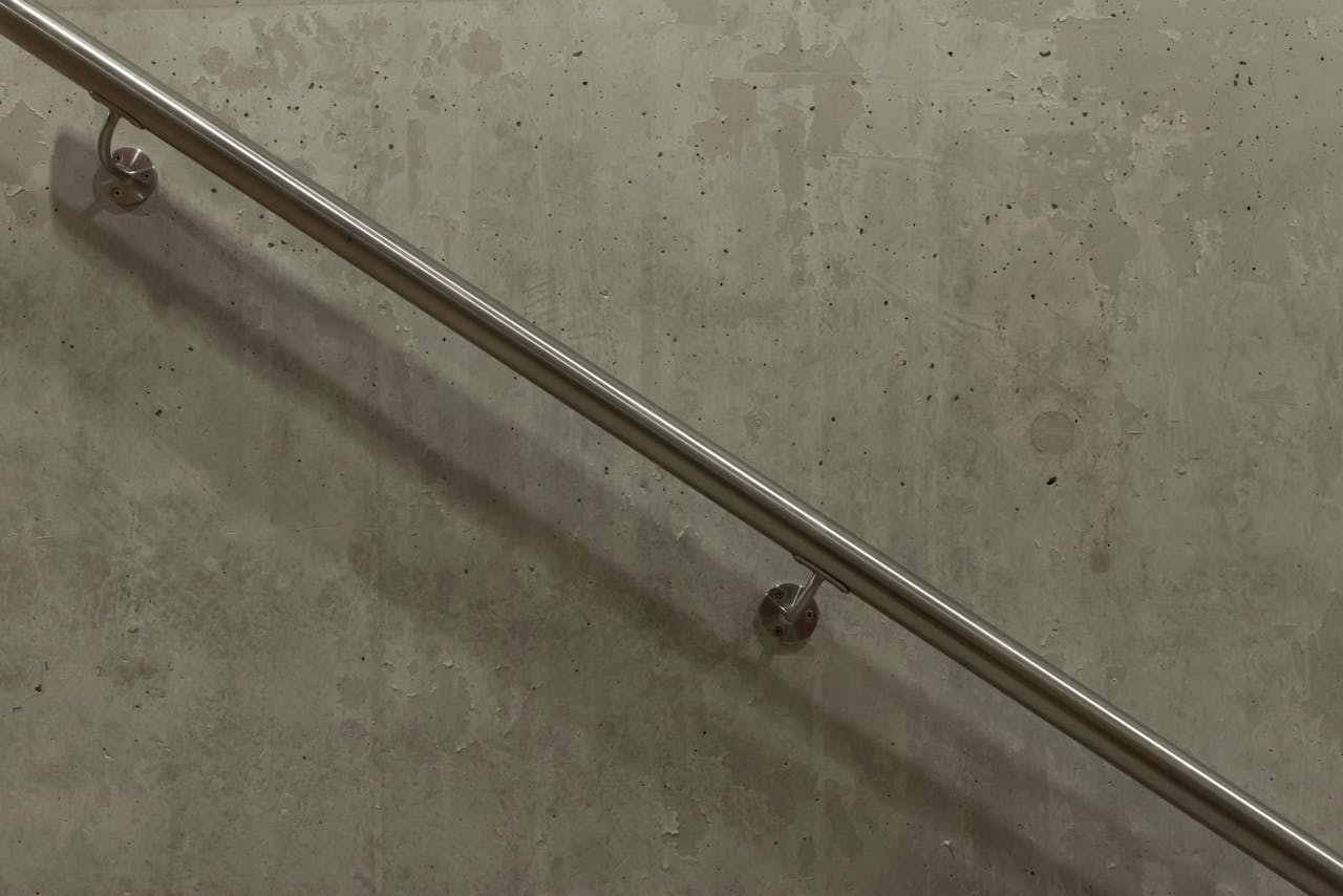 A minimalist image of a stainless steel handrail mounted on a concrete wall.